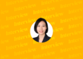 This image shows a professional portrait of Hyungyu Kang, Partner at Yulchon LLC, set against a bright yellow background with repeated “Interview” text in the backdrop, emphasizing the focus on her featured interview.